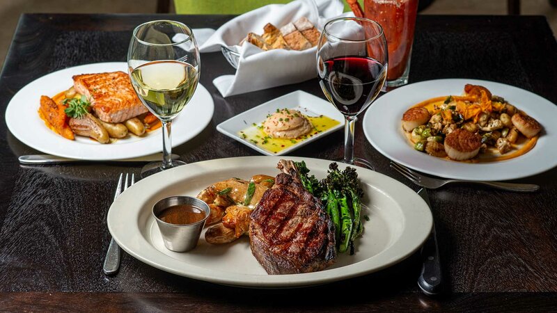 Multiple entrees with focus on steak with side of potatoes and asparagus